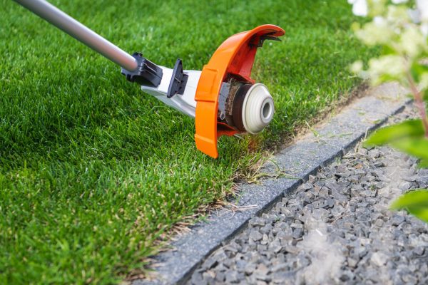A person trims the grass close to a stone edge using a grass trimmer, ensuring a neat garden appearance.